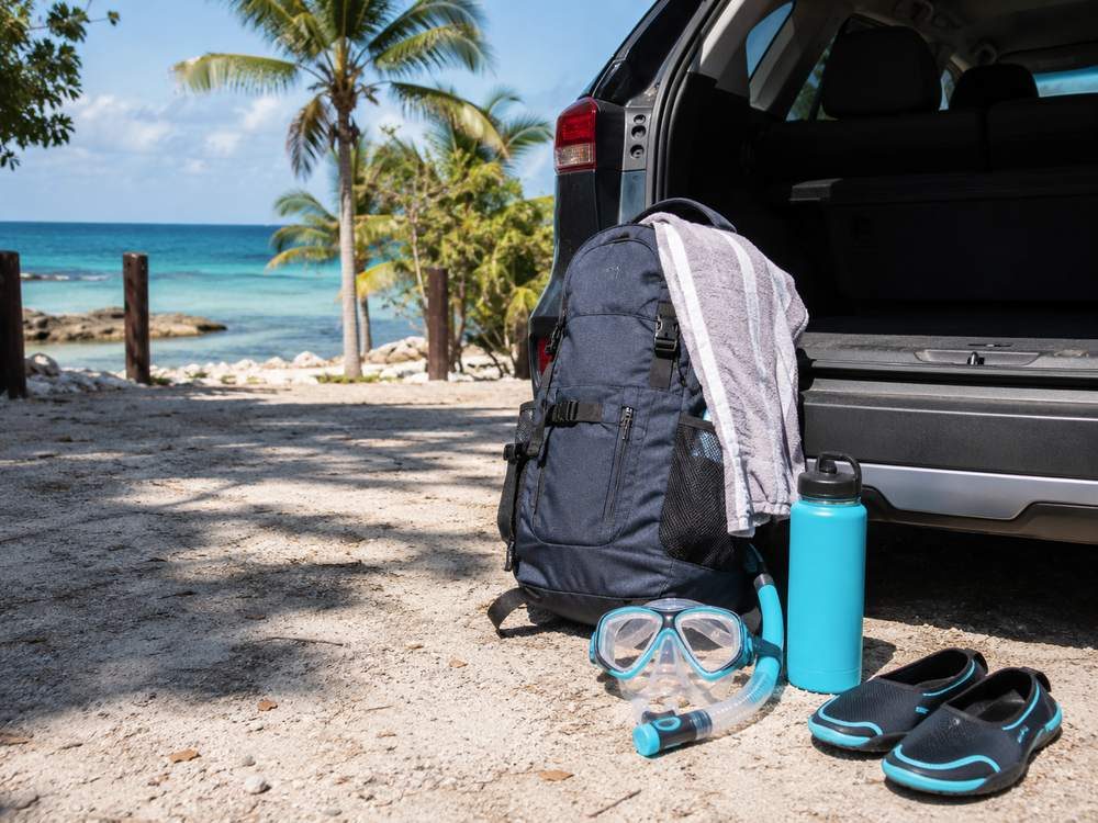 Day-trip backpack and snorkel gear beside a vehicle near the coast.