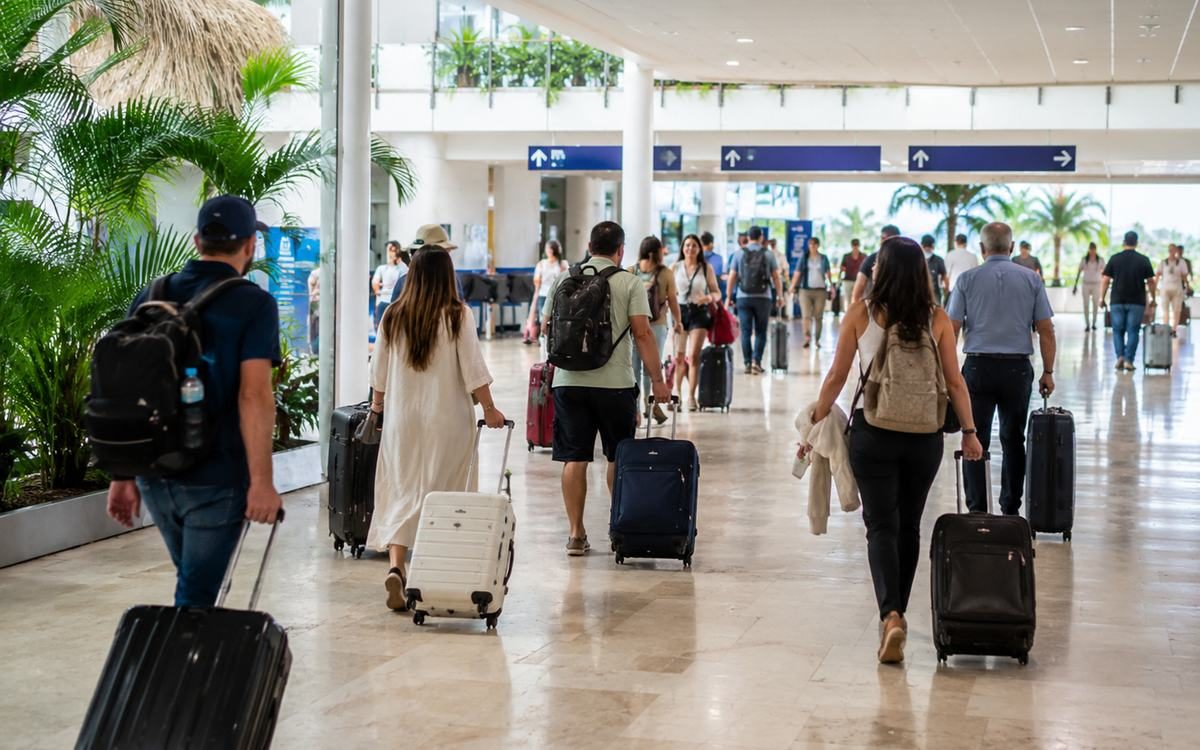Travelers walking through a busy airport arrivals corridor with luggage.