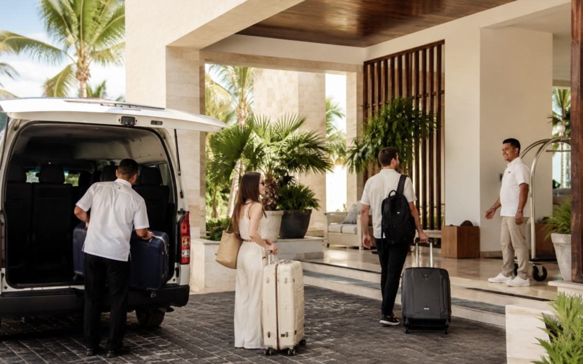Travelers arriving at a tropical hotel entrance with luggage after airport pickup.