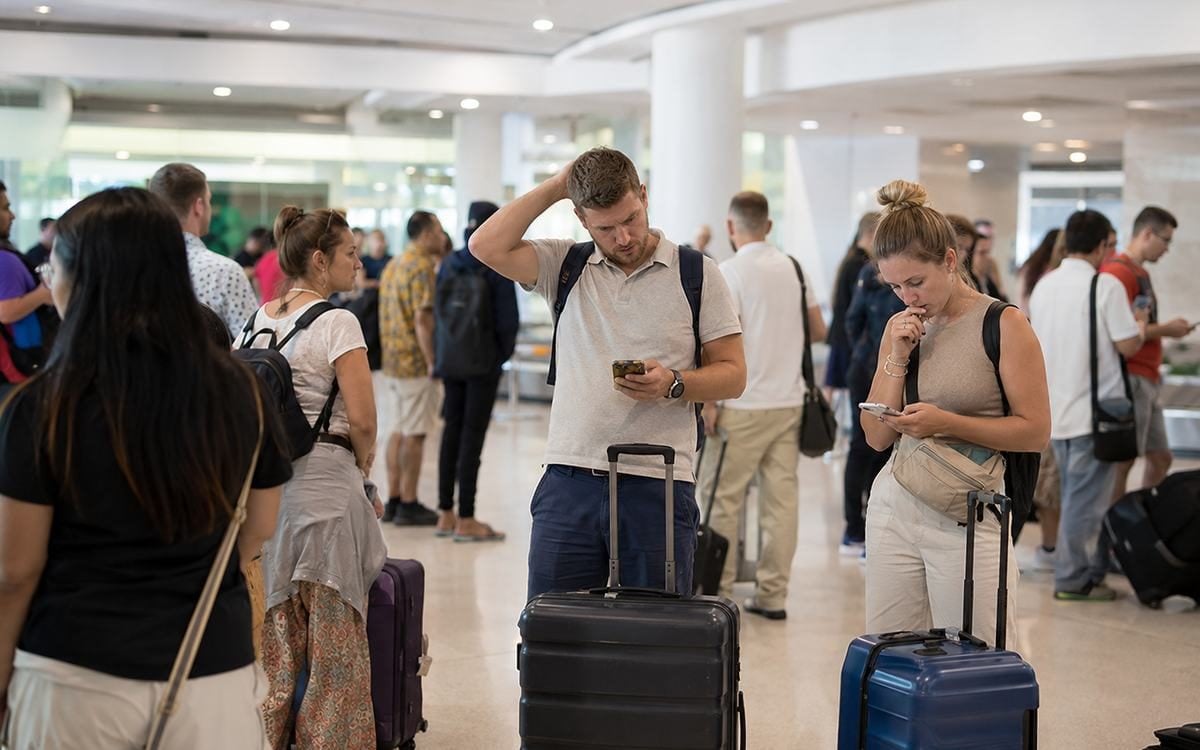 A busy airport terminal scene with travelers and luggage moving through the arrivals area.