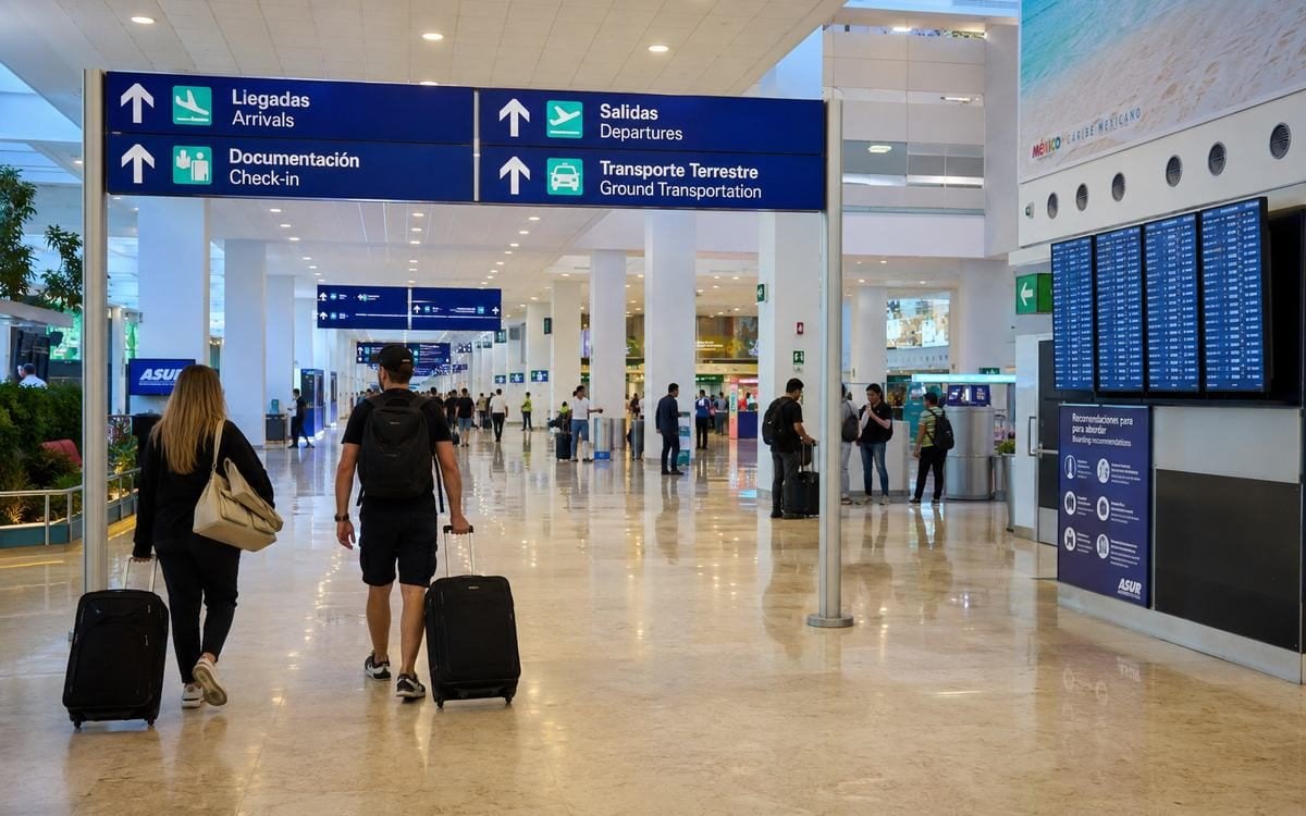 Travelers walking beneath interior terminal signs in a modern airport.