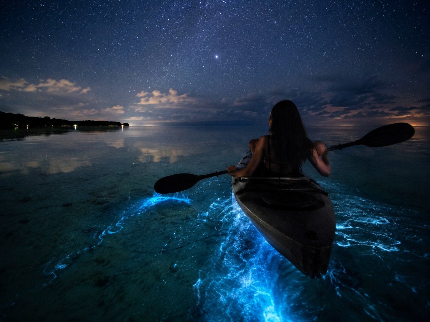 Subtle natural bioluminescent sparks around a hand moving through shallow water.