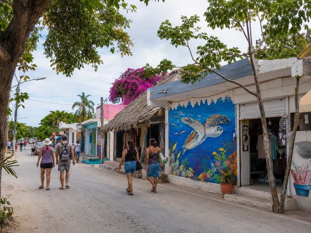 Akumal Pueblo mural street scene with local storefronts and pedestrians.
