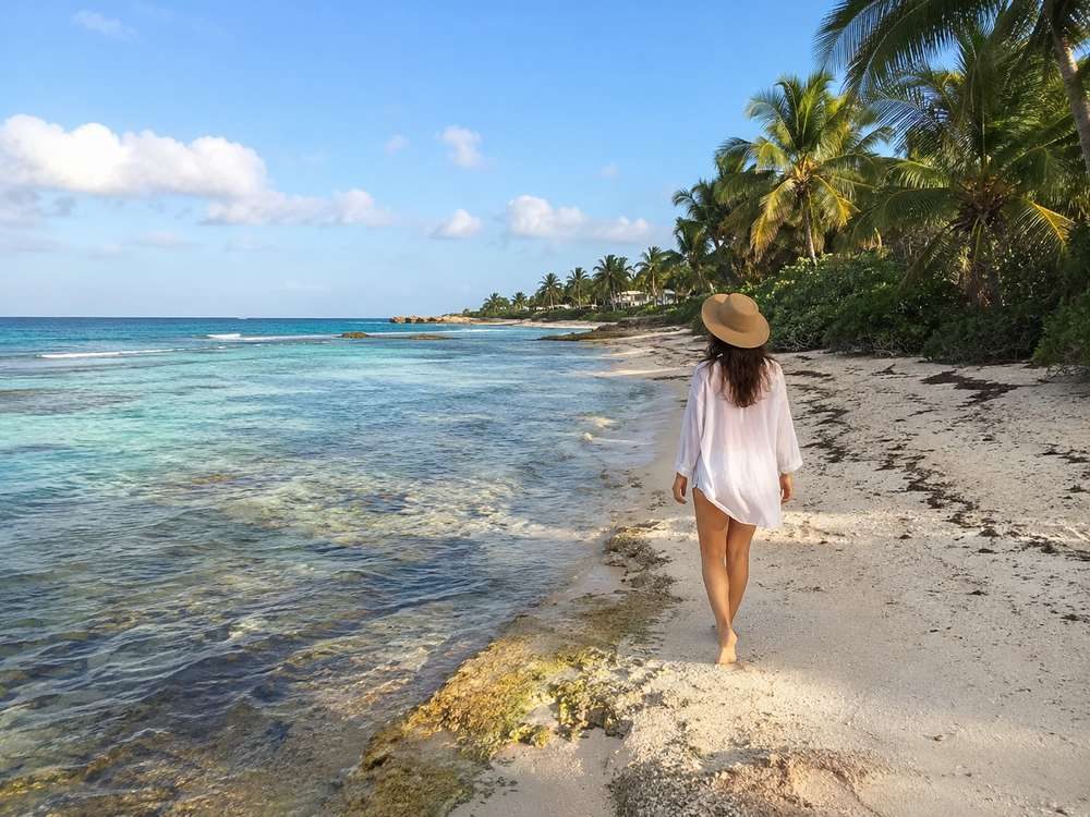Traveler walking beside a quiet Akumal shoreline with reef and palms visible.
