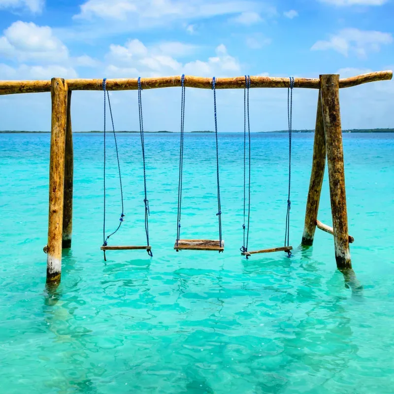 Three empty wooden swings standing in turquoise water