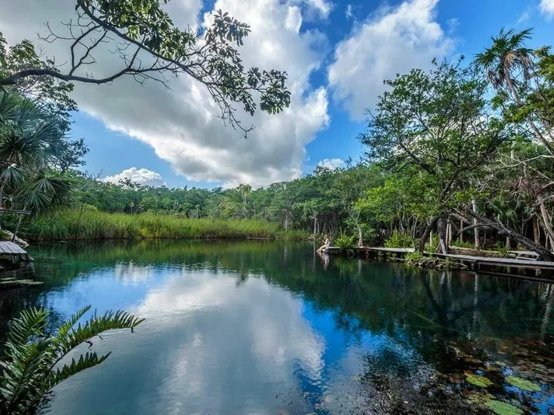 A calm freshwater lagoon reflecting jungle and clouds