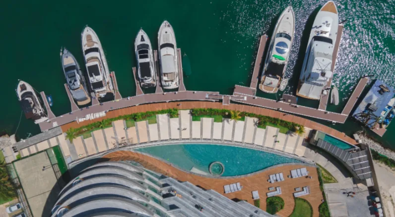Aerial view of a marina, boats and a curved oceanfront pool