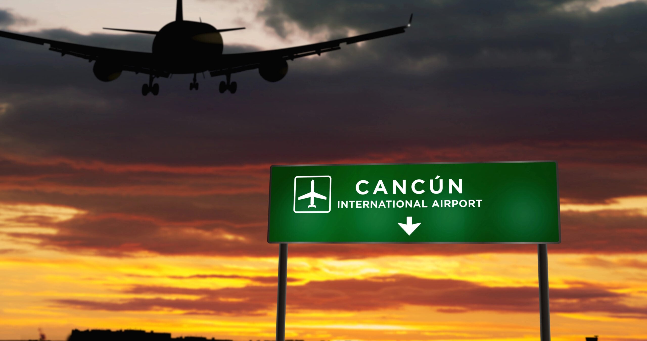 Cancún International Airport sign at sunset with an aircraft approaching overhead.